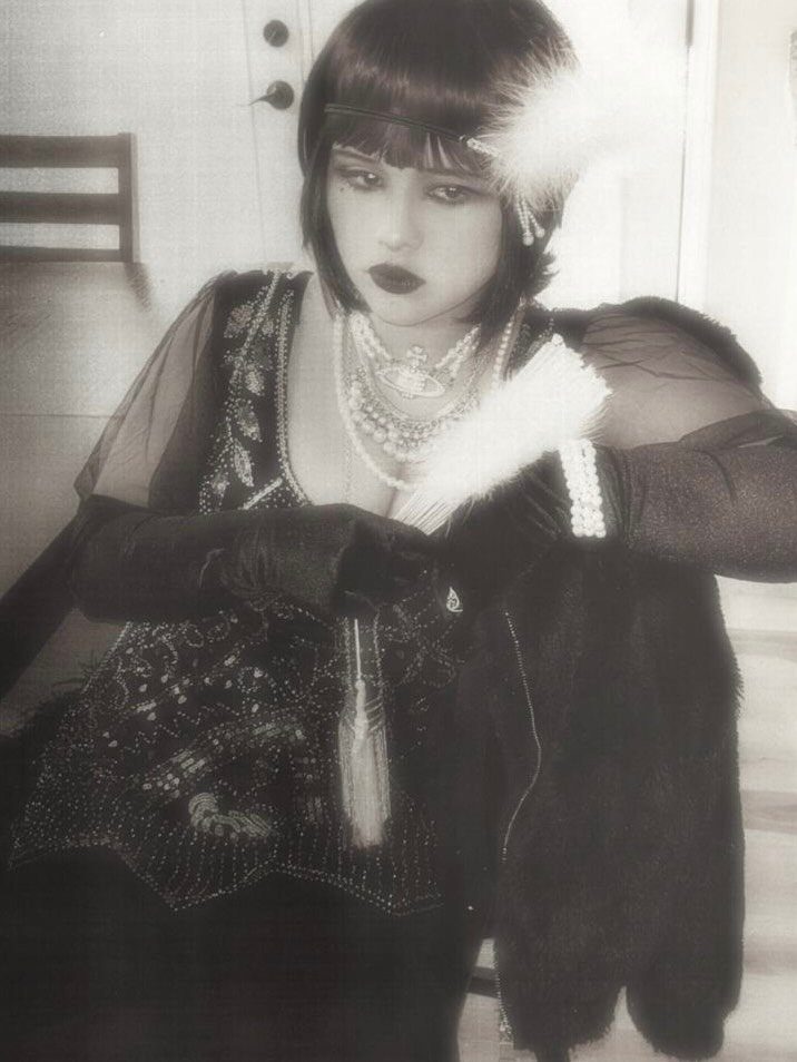 A woman dressed in vintage 1920s flapper style with pearls and a feather fan.