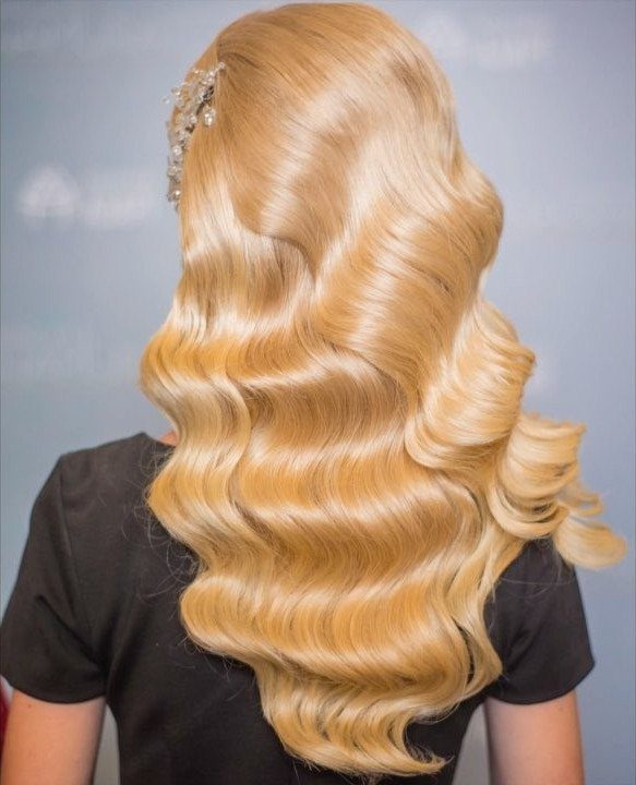Long blonde hair styled in deep, structured finger waves with a jeweled hair clip.