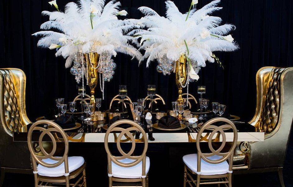 White ostrich feather centerpieces with crystals in gold vases on a formal dining table.