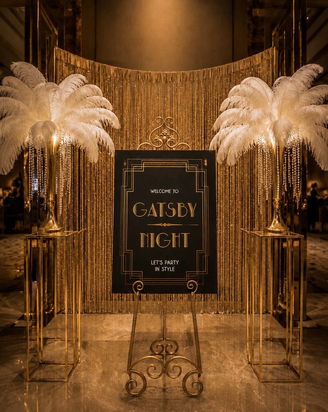 Gold Art Deco sign on an easel flanked by white ostrich feather centerpieces and gold tinsel.