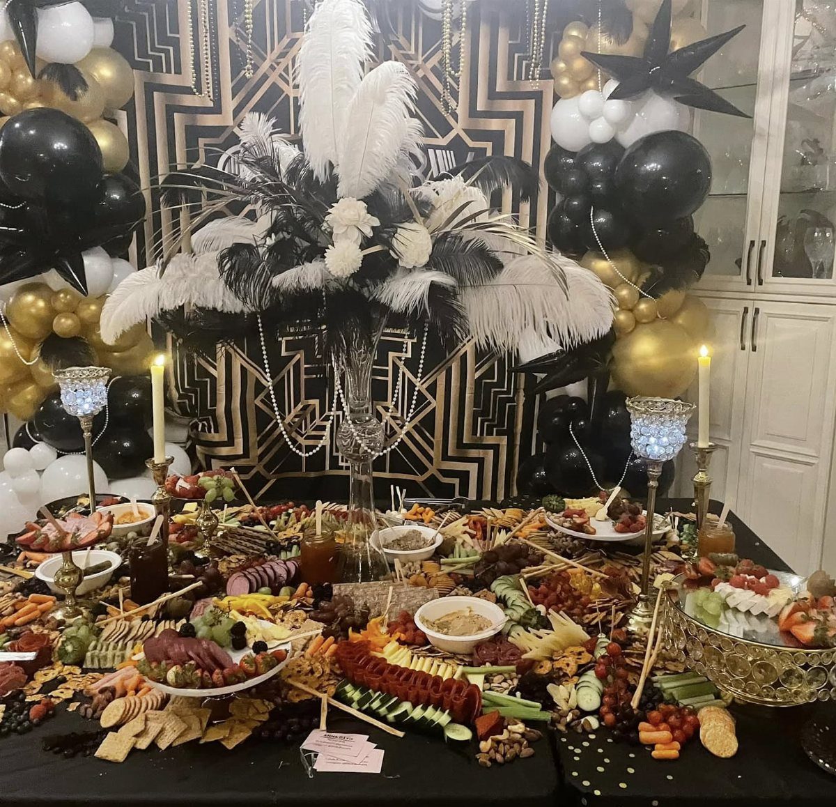 A large charcuterie spread on a table set against a black and gold Art Deco backdrop.