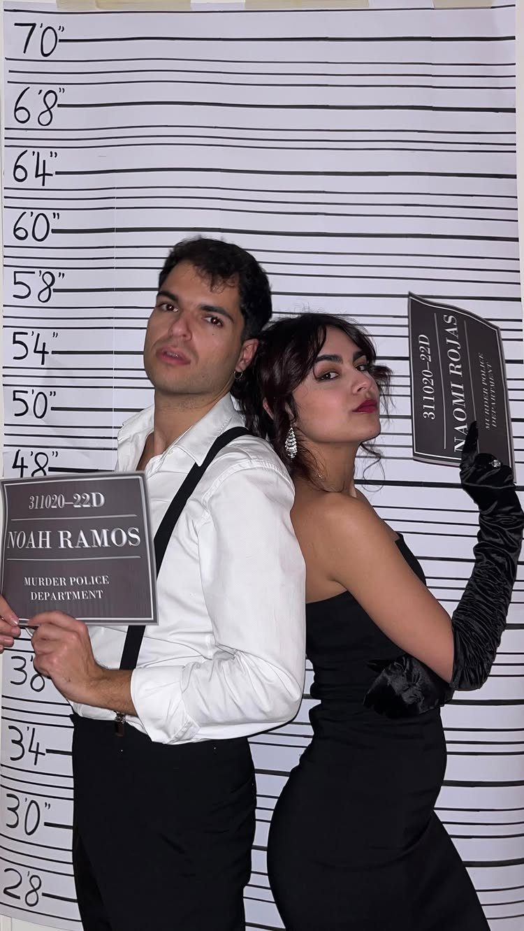 Man and woman posing back-to-back against a height chart holding police booking signs.