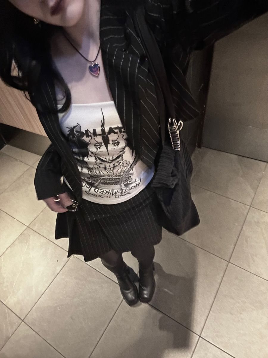 Person wearing a black pinstripe oversized blazer over a white graphic tank top and black skirt.