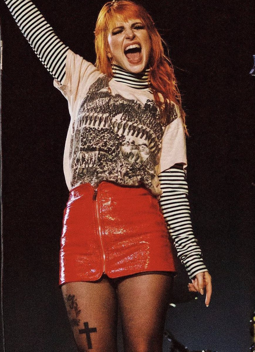 Woman with orange hair performing on stage in a graphic t-shirt and red skirt.