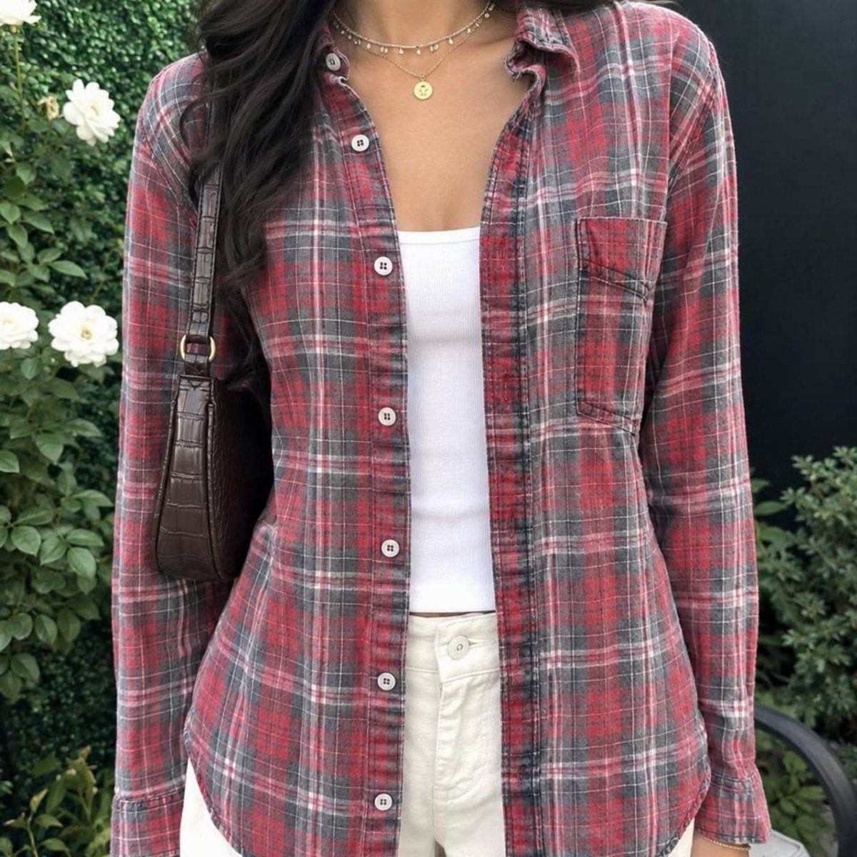 A person wearing a red and grey plaid button-down shirt layered over a white tank top.