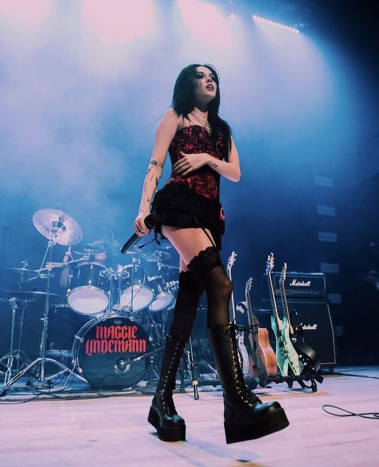 A female singer performing on stage wearing a lace corset top and platform boots.