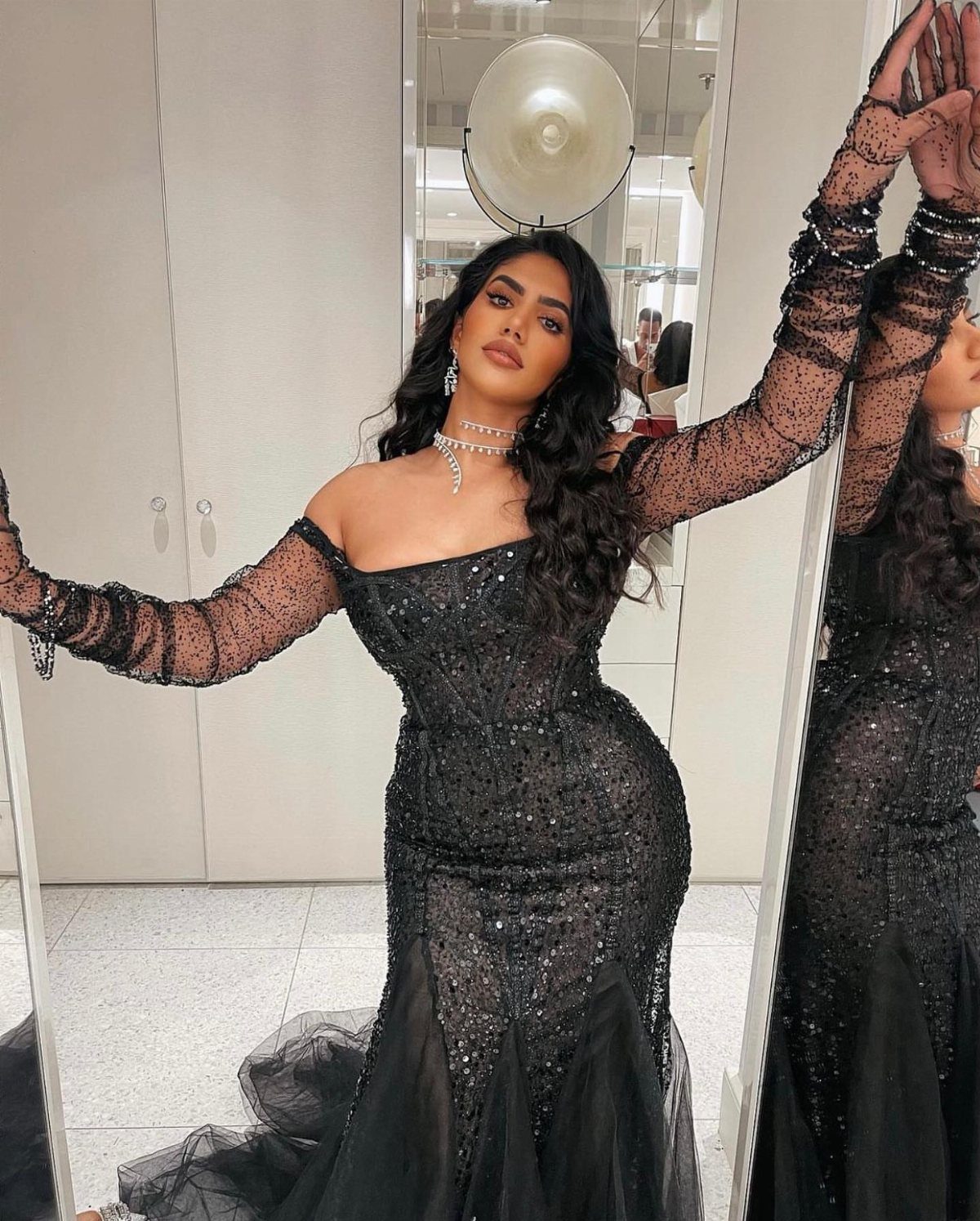 Woman in a black sequined mermaid gown posing in front of a mirror.