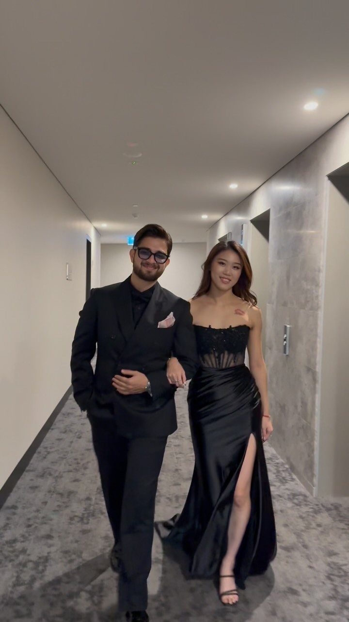 A man in a black tuxedo and a woman in a black formal gown walking down a hallway.