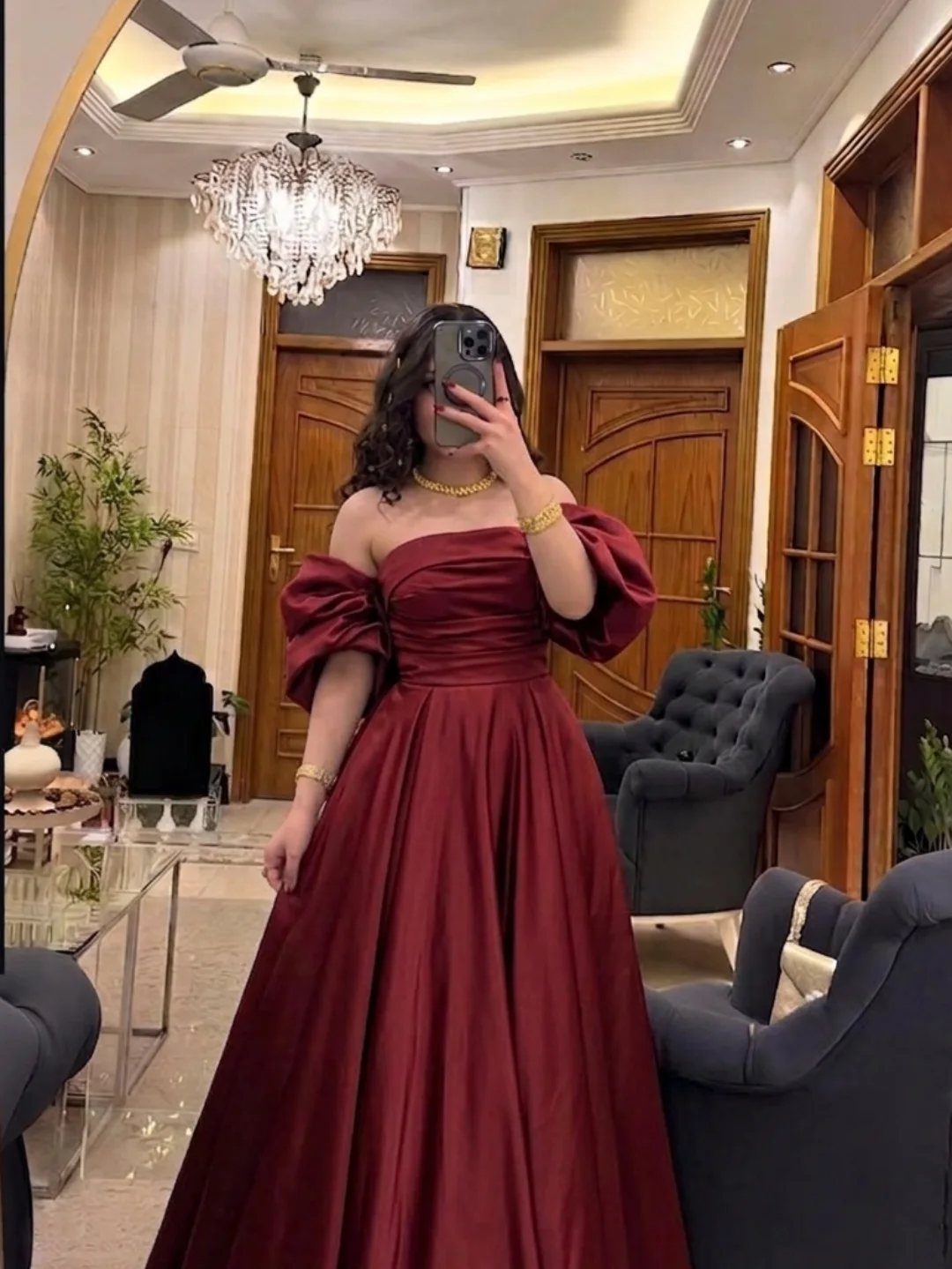 Woman in a red satin off-the-shoulder ball gown posing for a mirror selfie indoors.