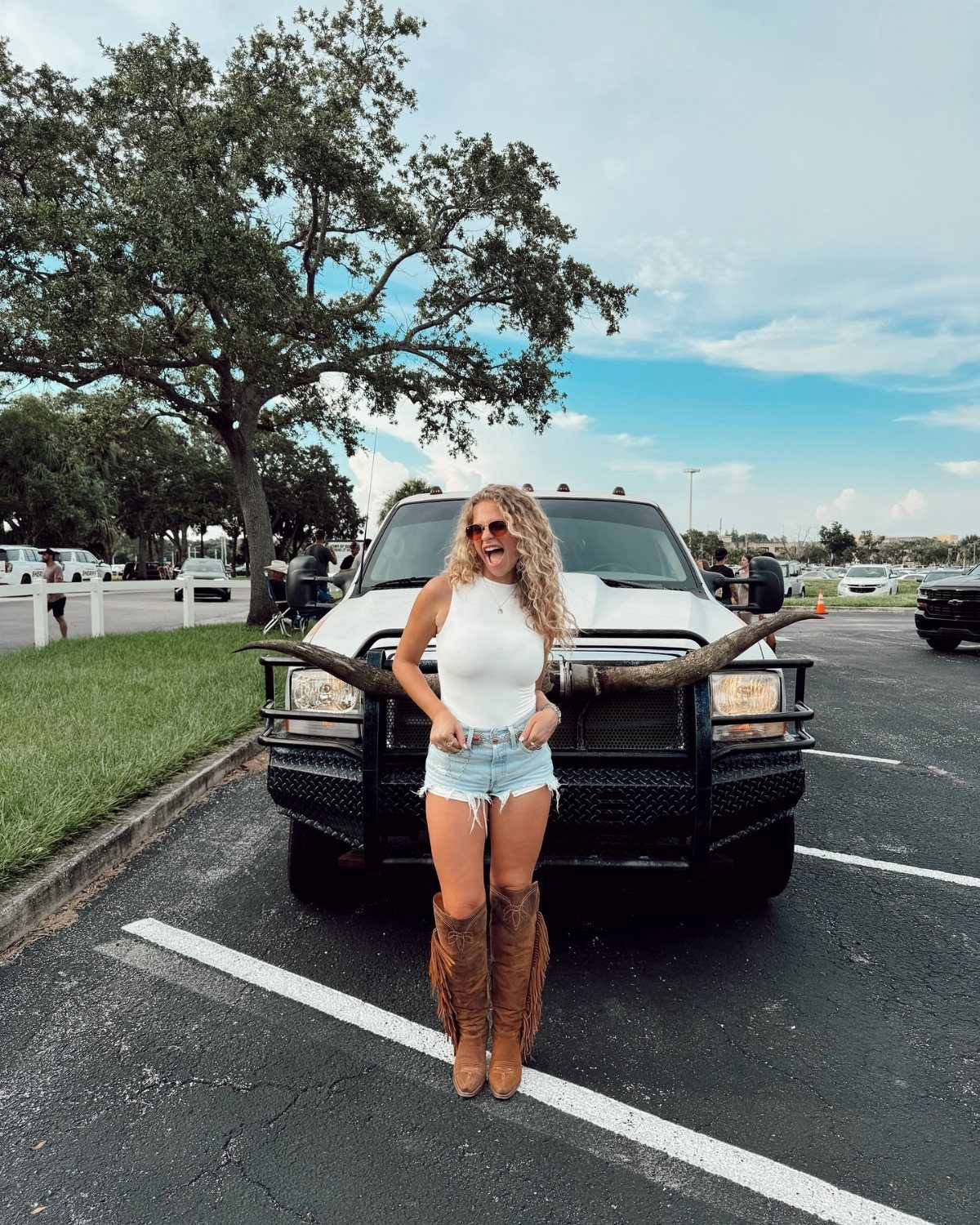 A woman in denim shorts and cowboy boots posing in front of a white truck.