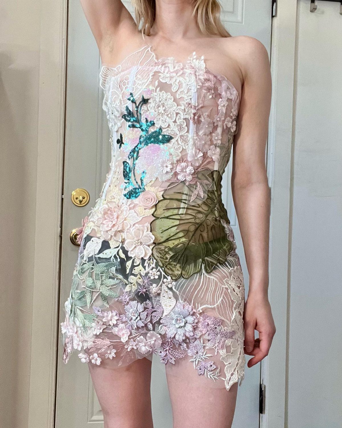 A person wearing a short, strapless dress made of sheer mesh with colorful floral lace appliqués.