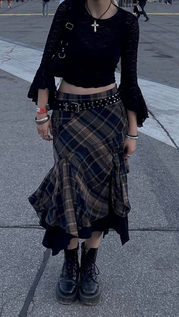 Person wearing a black lace top, plaid mermaid skirt, studded belt, and black combat boots.