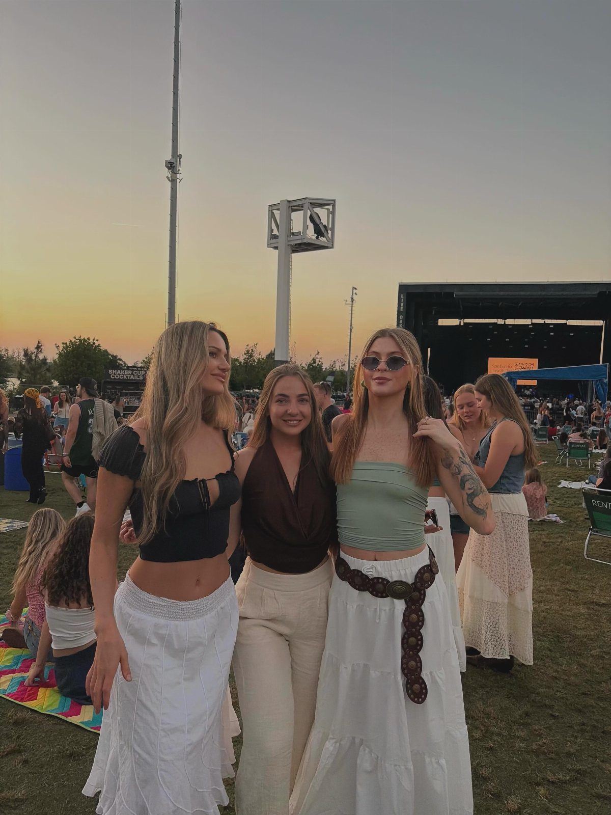 Three young women posing together in a grassy field during a sunset outdoor event.