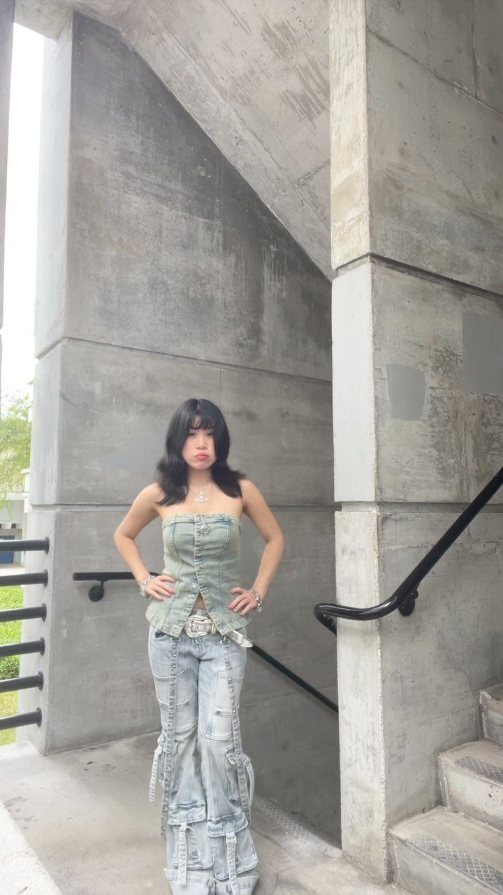A woman posing in a concrete stairwell wearing a denim corset and baggy denim cargo jeans.