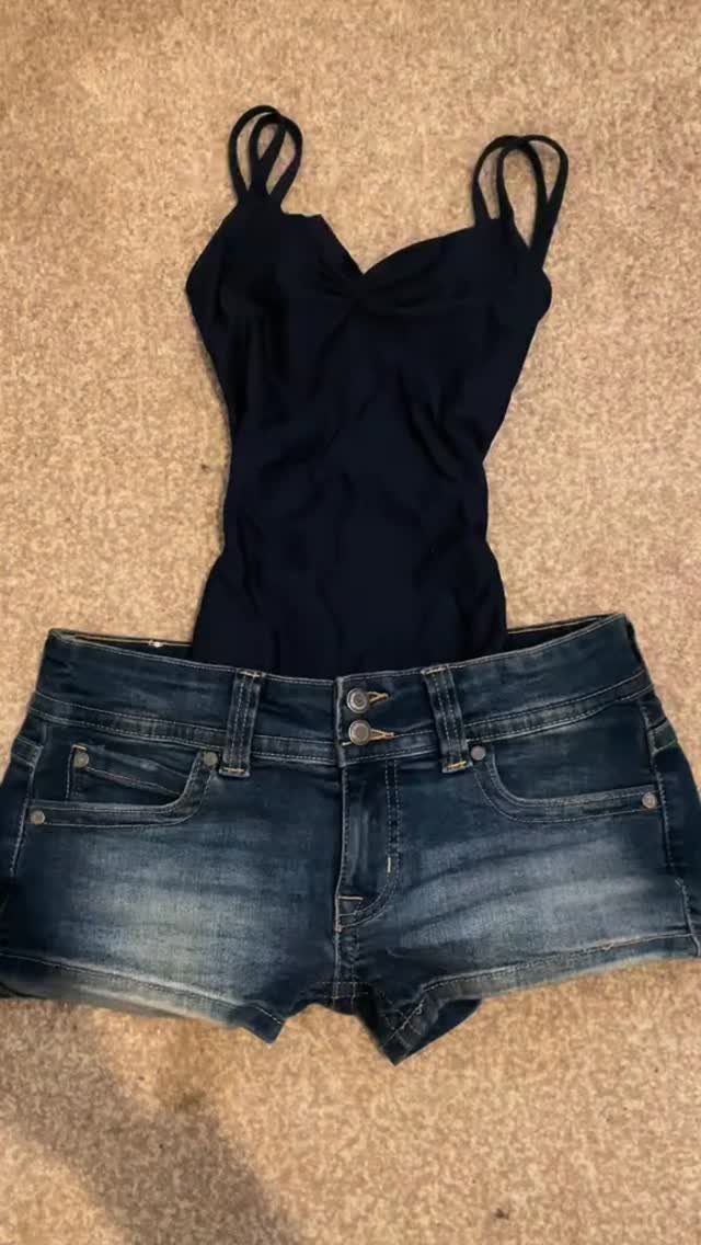 Black spaghetti strap tank top and blue denim shorts laid flat on a beige carpet.