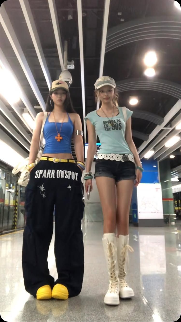 Two women posing in a subway station wearing colorful Y2K style streetwear outfits.