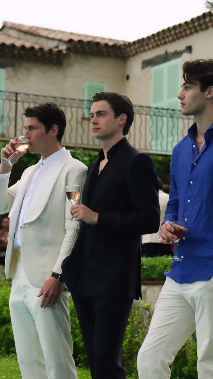 Three men in stylish summer attire standing together in an outdoor garden setting.