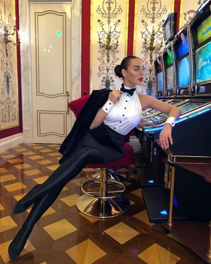 Woman wearing a white tuxedo-style top and black bow tie sitting in a casino.