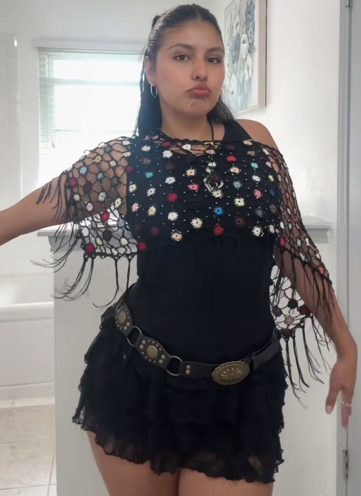 A woman posing in a black bodysuit, ruffled skirt, and a decorative crochet capelet.
