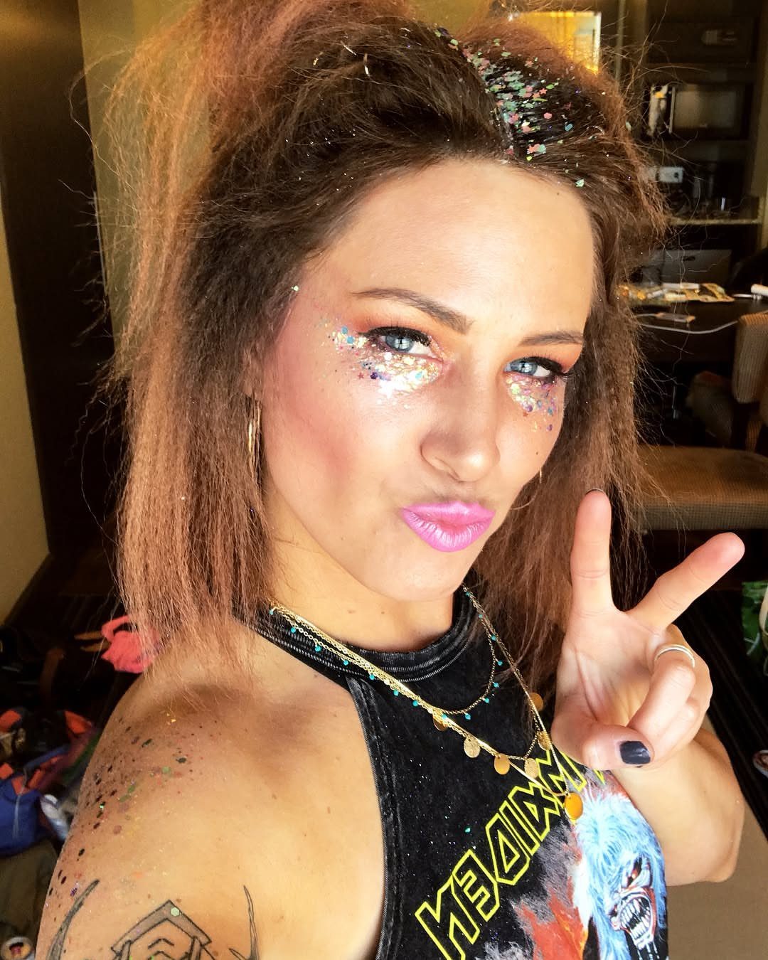 A woman with textured hair and glittery makeup posing with a peace sign.