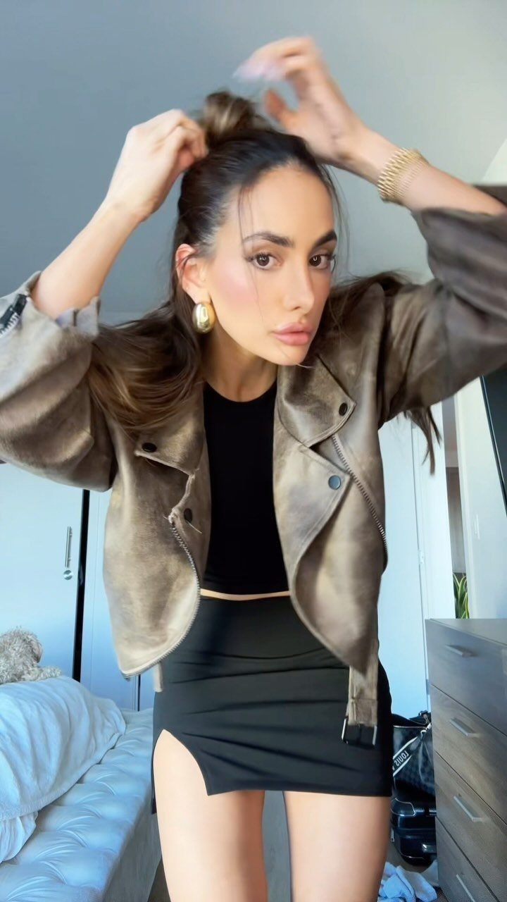 Woman wearing a black outfit paired with a metallic bronze jacket and gold jewelry.