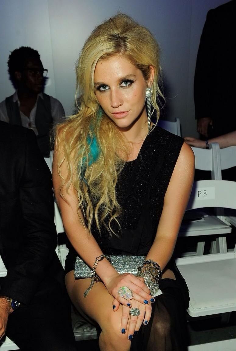 Blonde woman with long textured waves and a blue hair streak looking at the camera.