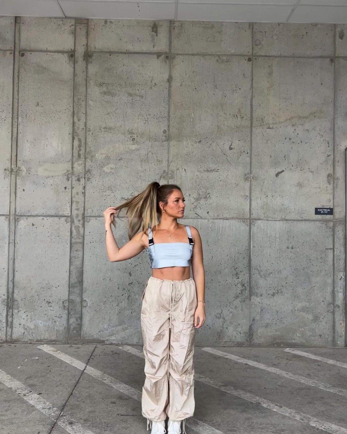Woman in a light blue crop top and beige cargo pants standing against a concrete wall.