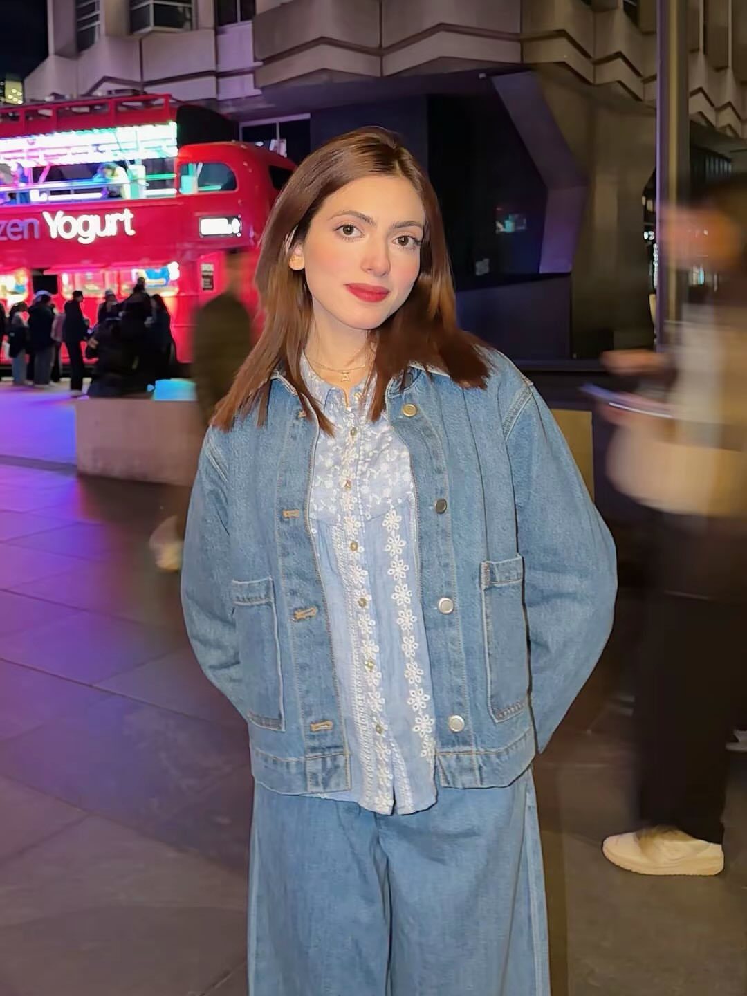 A woman wearing a denim jacket and lace blouse posing in a city at night.