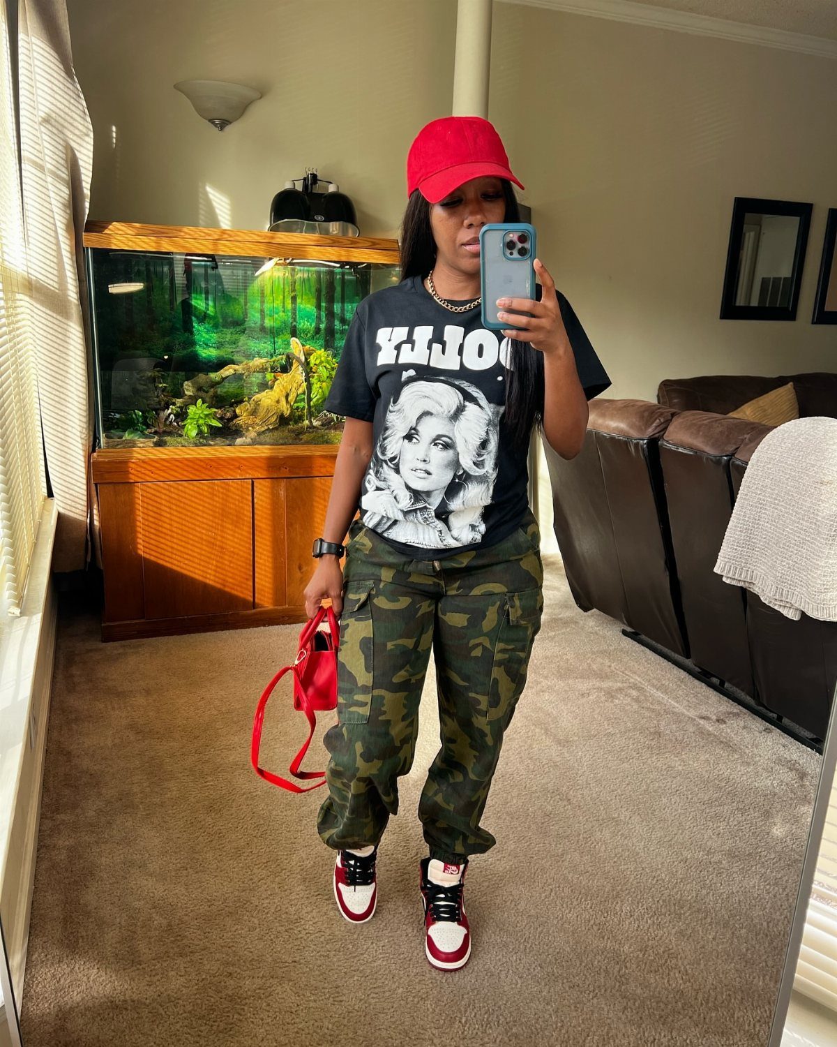 Woman in camouflage cargo pants, a black graphic t-shirt, and a red cap taking a selfie.
