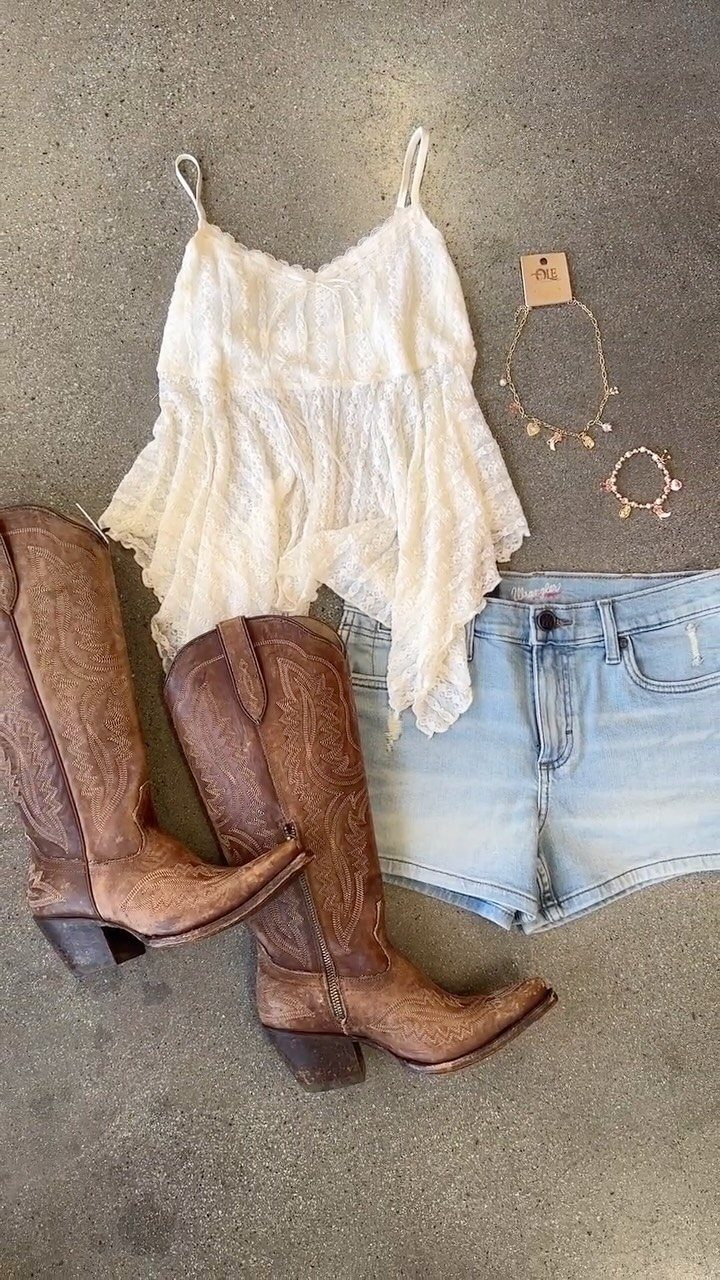 White lace camisole, denim shorts, brown cowboy boots, and gold necklaces laid on concrete.