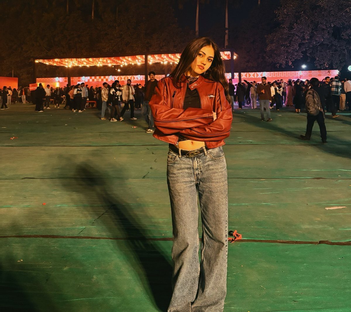 Woman posing in a red leather jacket and blue denim jeans at an outdoor night event.