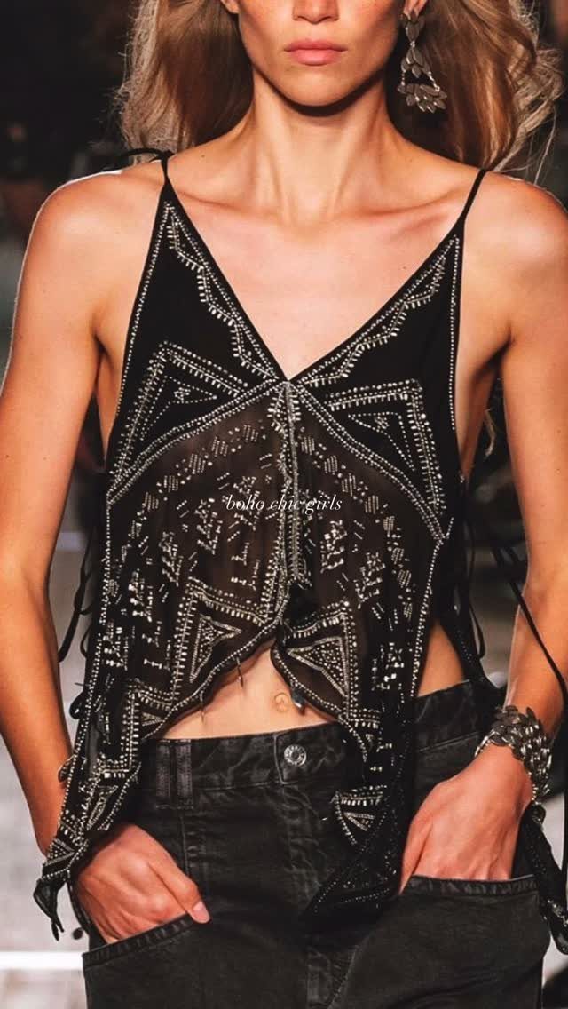 A person wearing a black rhinestone-embellished sheer camisole and black denim pants.