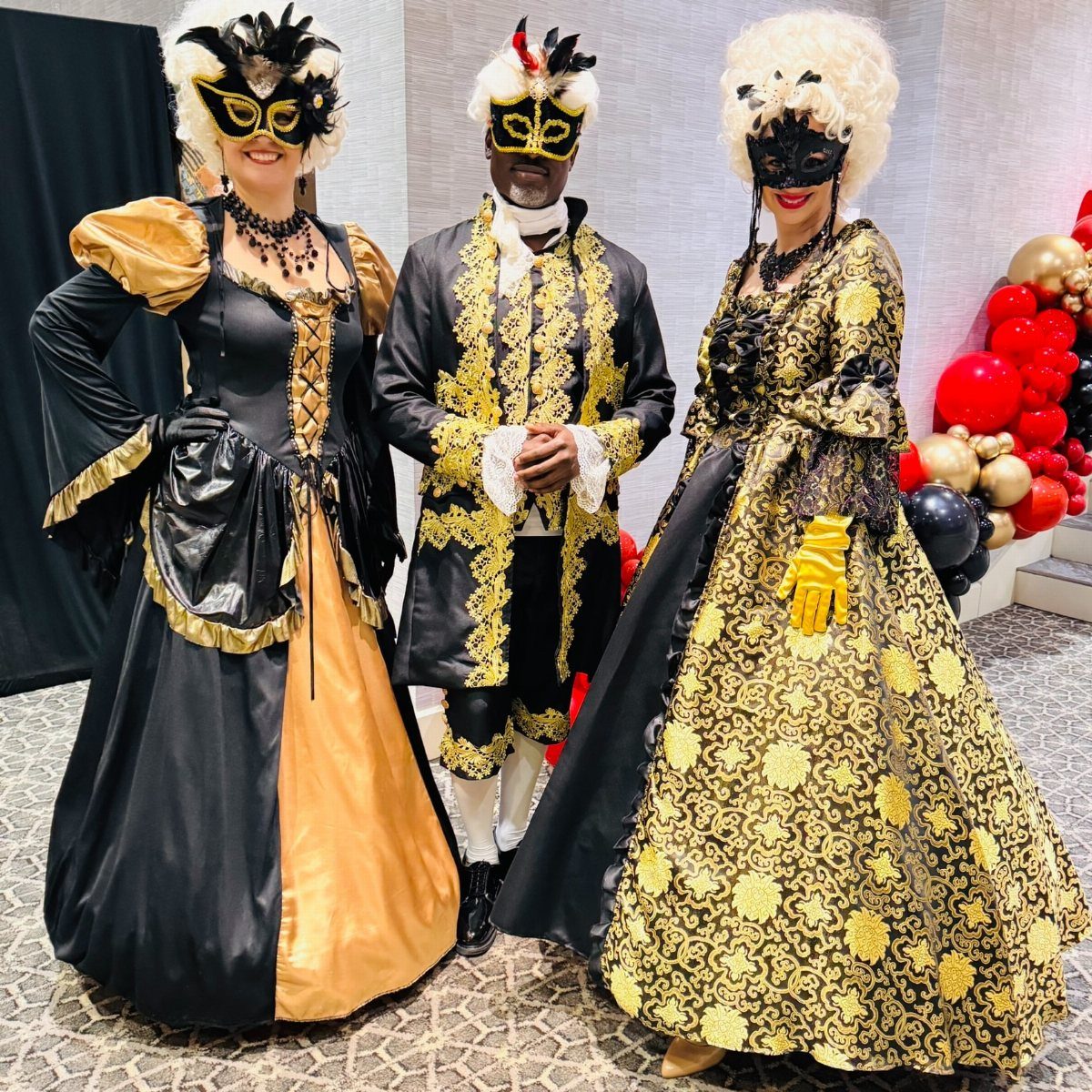 Three people wearing elaborate gold and black masquerade costumes and ornate masks.