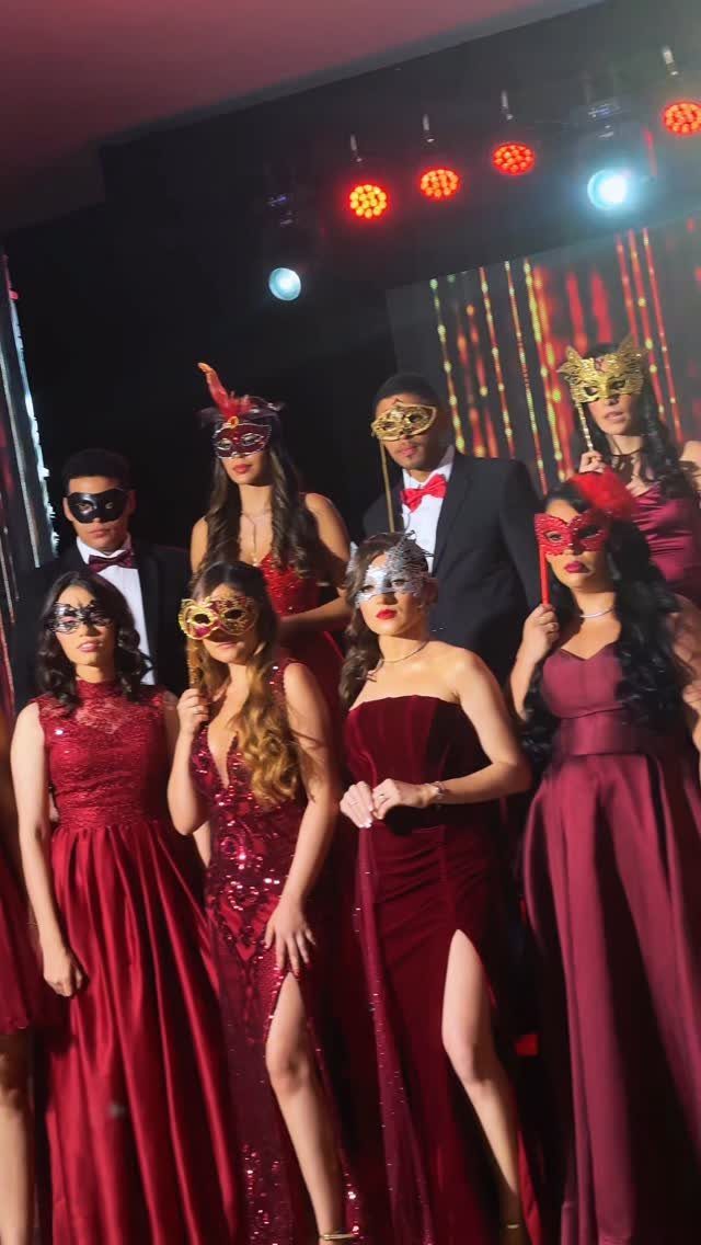 Group of people in formal red gowns and black suits wearing decorative masquerade masks.