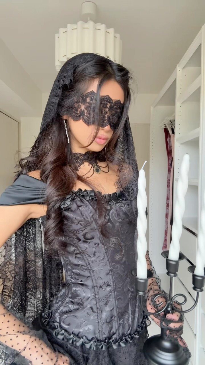Woman in a black lace gothic dress and matching lace mask posing with a candelabra.