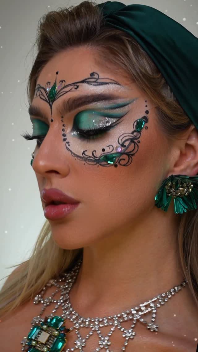 Woman with green masquerade mask style eye makeup and emerald jewelry.