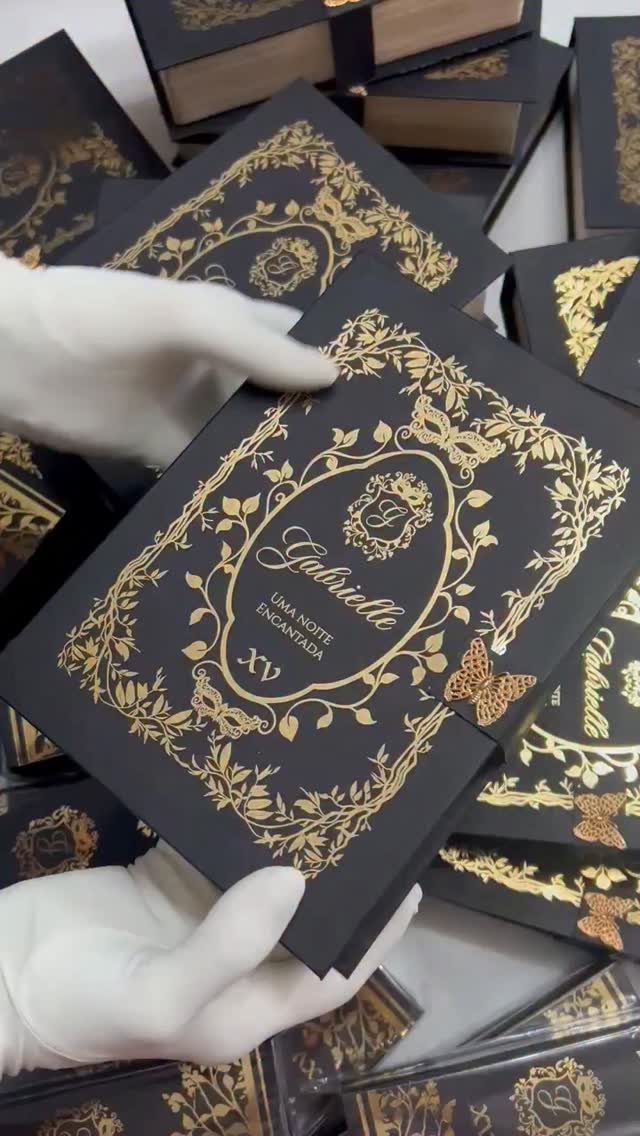 Hands in white gloves holding a black and gold floral patterned elegant invitation.
