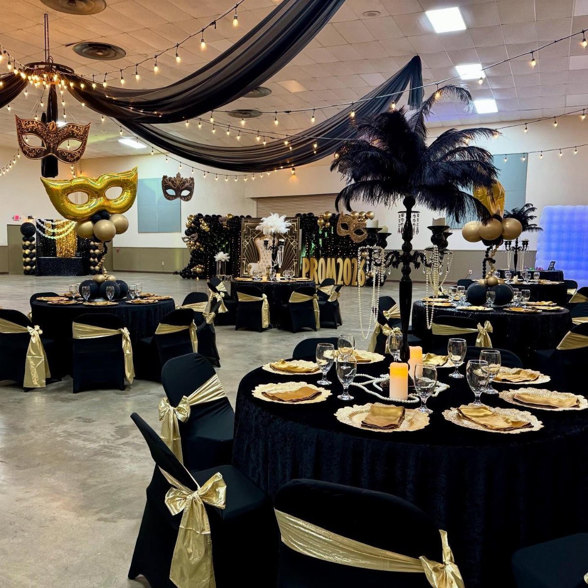 A ballroom decorated for a masquerade event with black and gold tables and ceiling drapes.