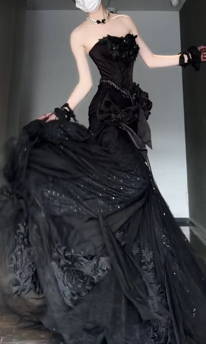 A person wearing an elaborate, sparkling black strapless ball gown with floral lace details.