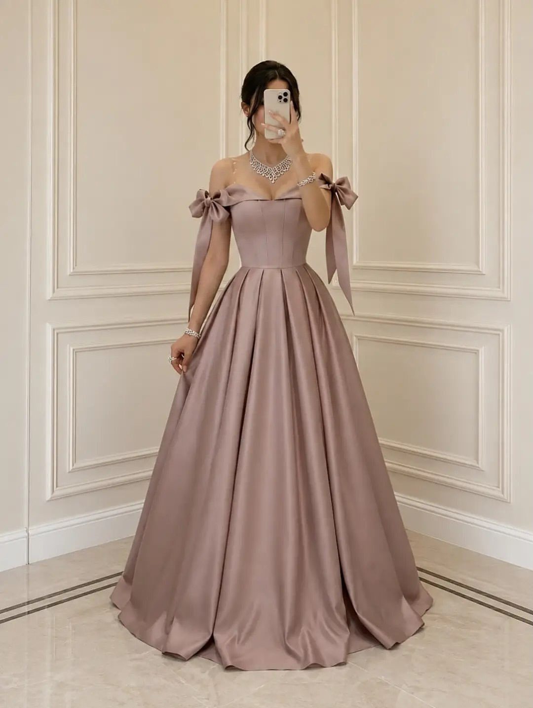 Woman in a mauve satin ball gown posing for a mirror selfie against white walls.