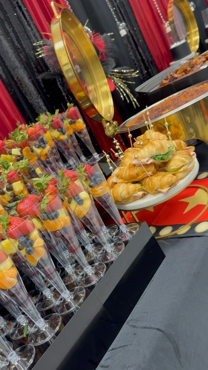 Fruit skewers in champagne flutes and small croissants arranged on a catering table.