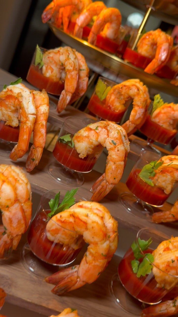 Small glasses of shrimp cocktail with red sauce and parsley garnishes arranged on a table.