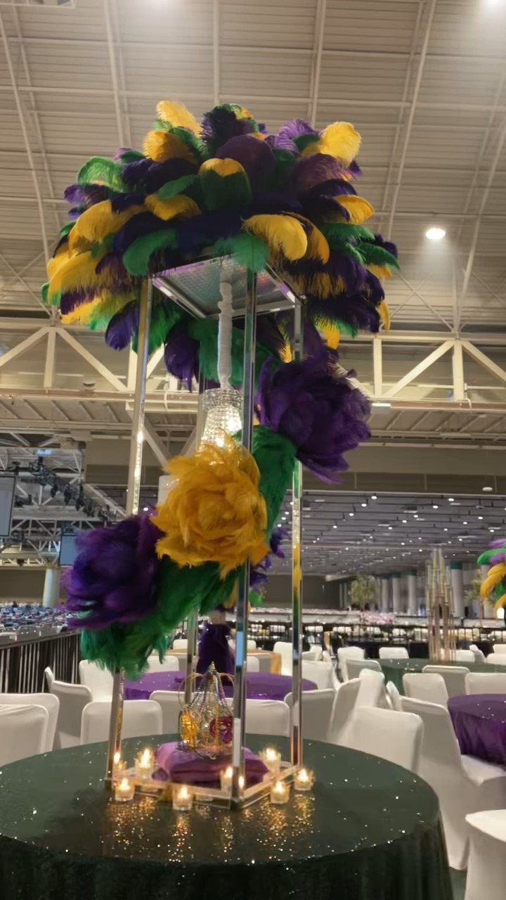 Large purple, yellow, and green feathers decorating a tall silver centerpiece on a banquet table.