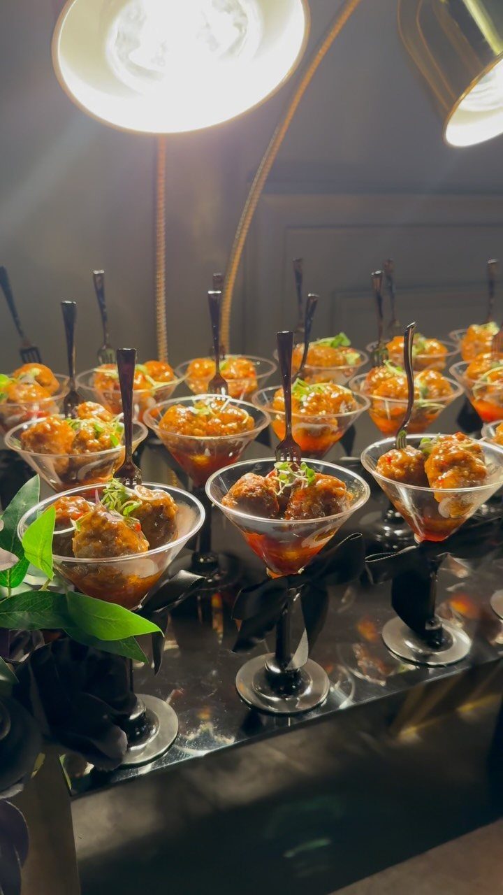 Small savory appetizers served in martini glasses with orange sauce and green garnishes.