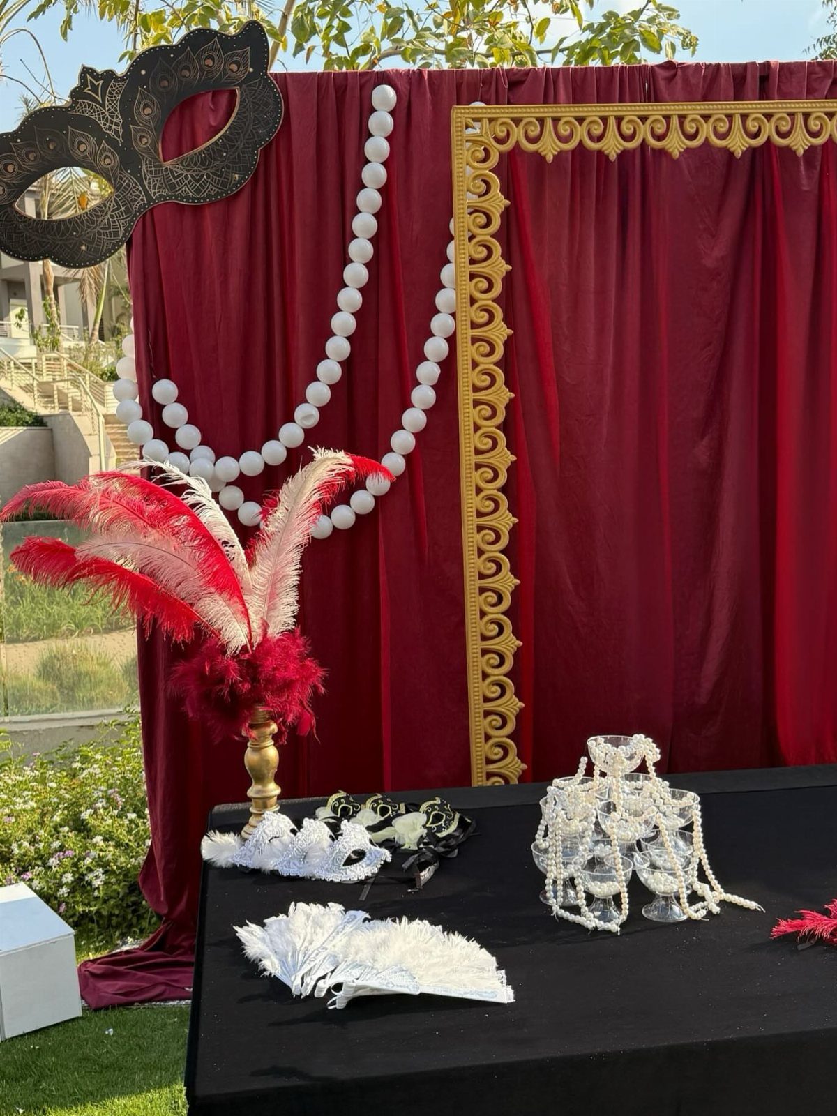 Masquerade decorations including a large black mask, red feathers, and white beads against red velvet.