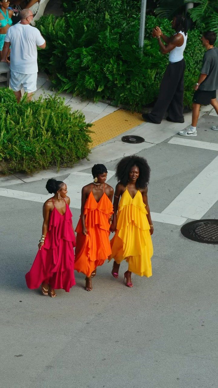Three women walking in bright pink, orange, and yellow tiered flowy maxi dresses.