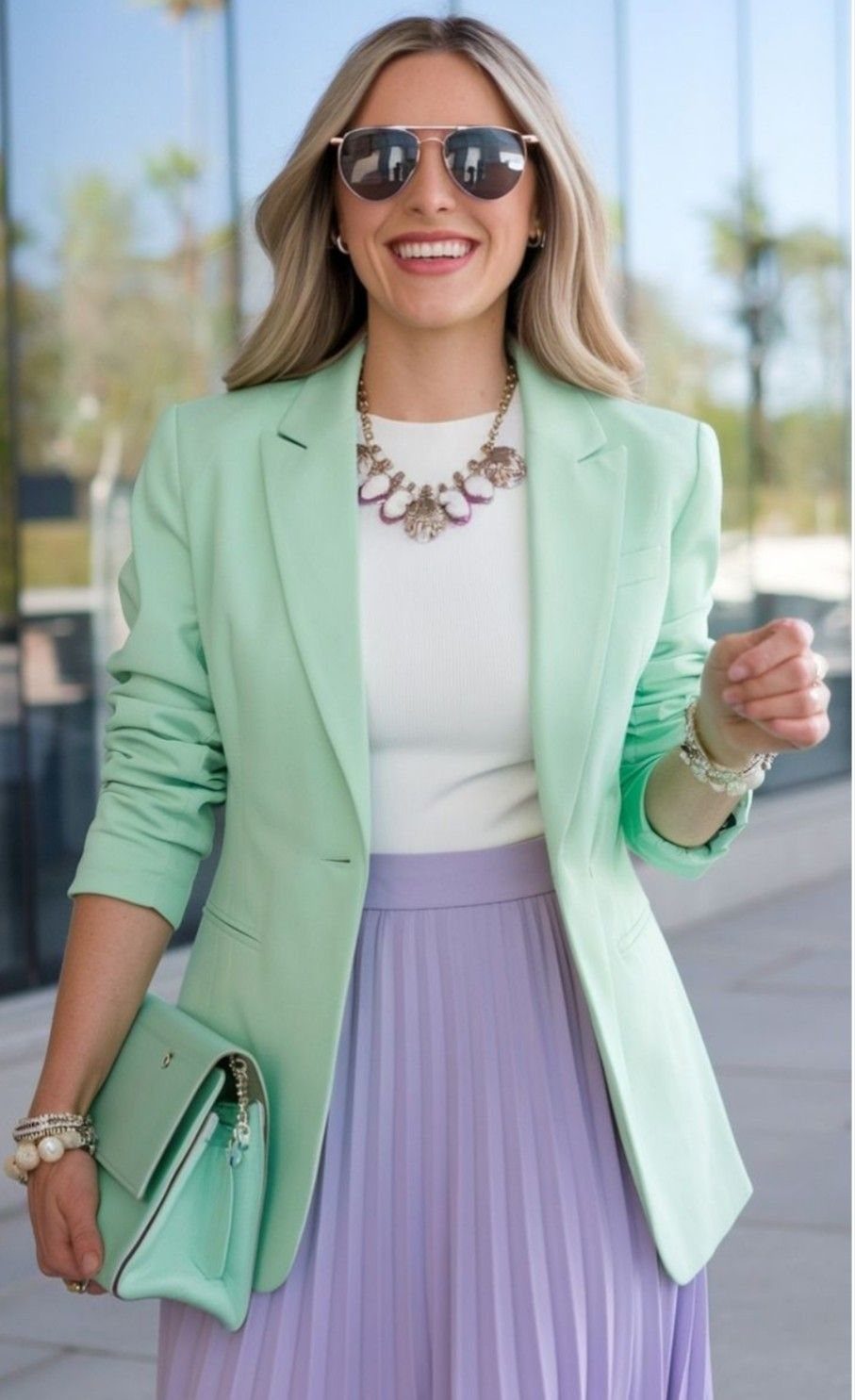 A smiling woman wearing a mint green pastel blazer and a lavender pleated skirt.