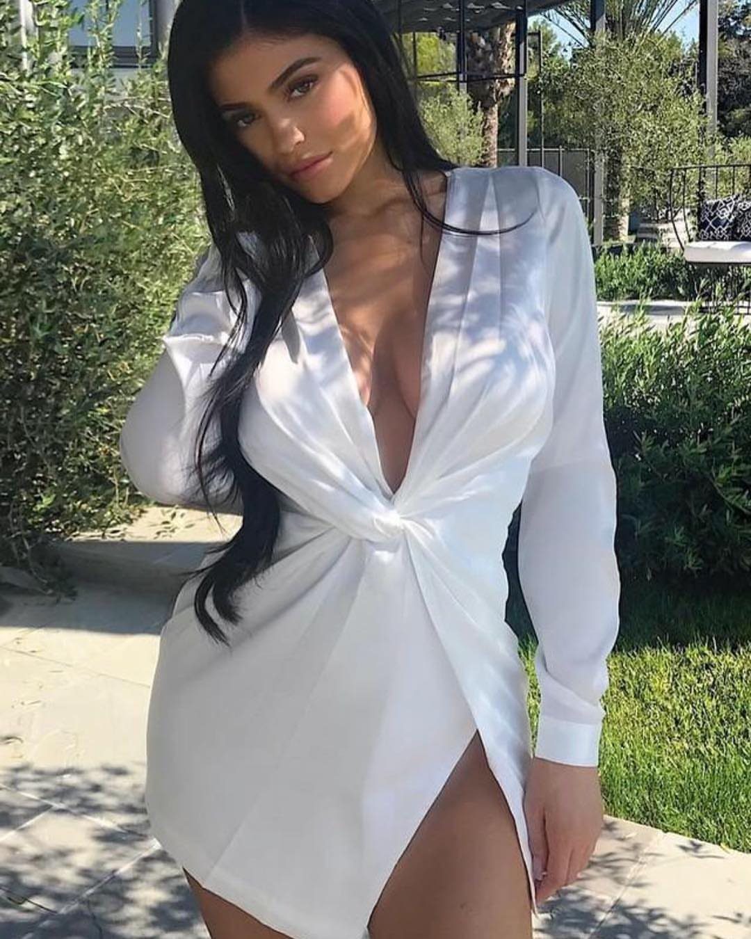 A woman posing in a white long-sleeved satin mini dress with a deep neckline.