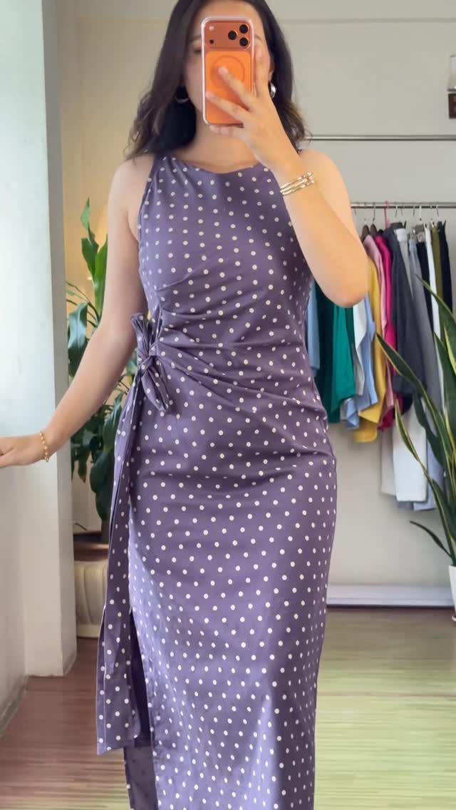 Woman in a long purple sleeveless dress with white polka dots taking a mirror selfie.