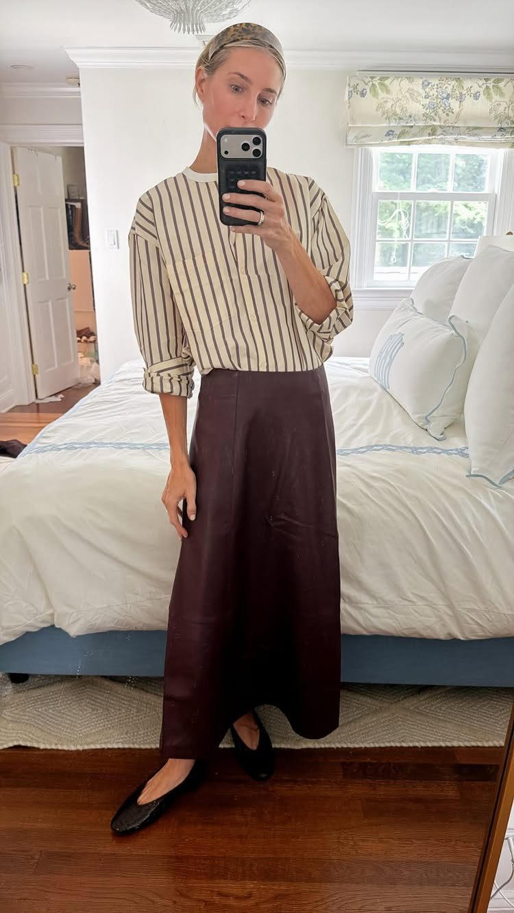 Woman in a striped blouse and long dark brown skirt posing for a mirror selfie.